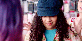 a woman with curly hair wearing a blue hat and a floral shirt is smiling .