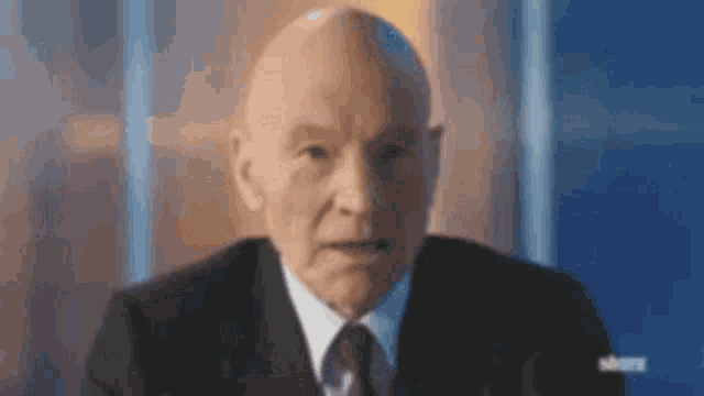 a bald man in a suit and tie is looking at the camera with a serious look on his face .