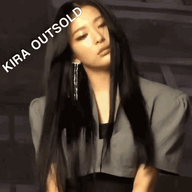 a woman with long black hair is standing in front of a sign that says kira outsold on it