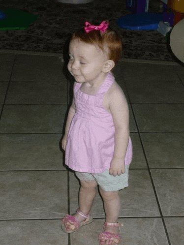 a little girl wearing a pink top and shorts is standing on a tile floor