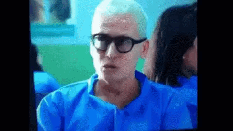 a man wearing glasses and a blue shirt is sitting in a room .