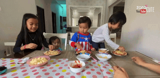a group of children are sitting at a table with plates of food in front of a sign that says " zora pim "