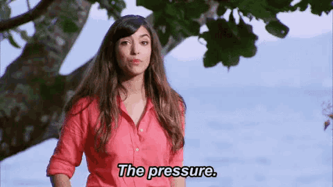 a woman in a red shirt is standing in front of a tree and says the pressure .