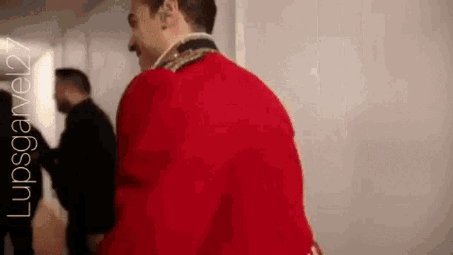 a man in a red jacket is standing in a hallway with other people .