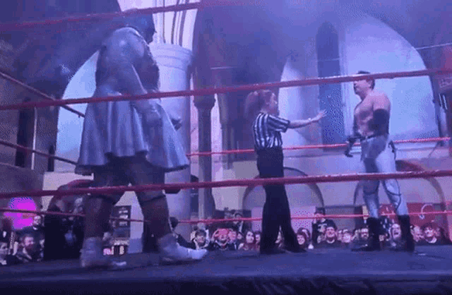 a referee stands in a ring with two wrestlers