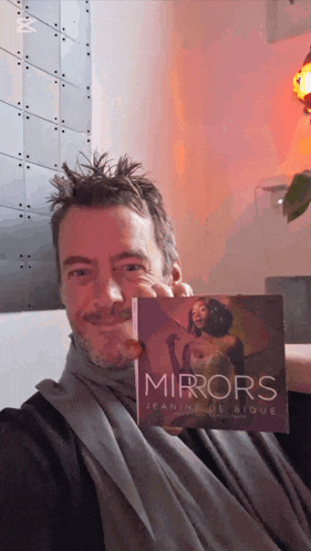 a man holding a book titled mirrors by jeanne de bique