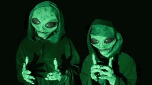 a couple of aliens in hoodies are standing next to each other in the dark .