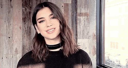 a woman wearing a choker and a sweater is standing in front of a window and smiling .