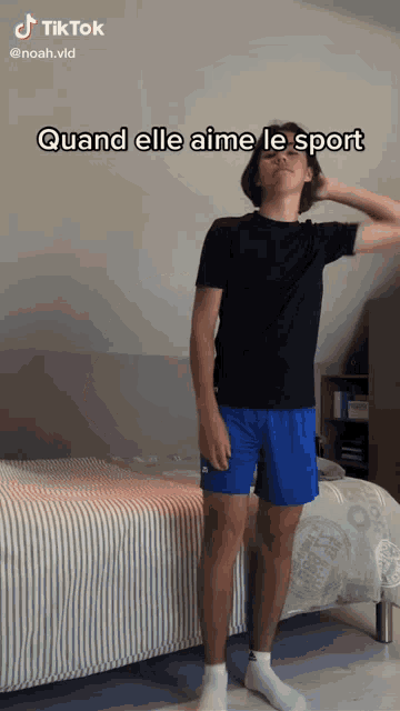 a man in a black shirt and blue shorts is standing in front of a bed with tiktok written on the bottom
