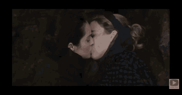 two women kissing on a screen with a play button below them