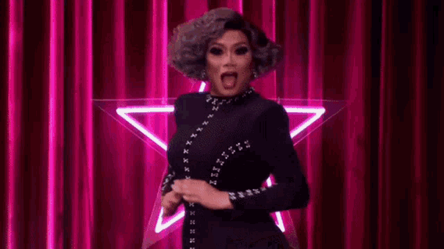 a drag queen is standing on a stage in front of a pink curtain with the words `` juj u bff '' .
