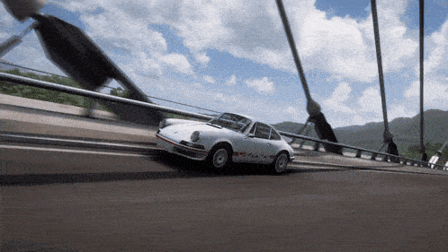 a white porsche is driving over a bridge with mountains in the background