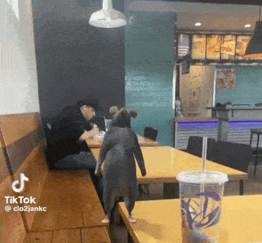 a man sits at a table in a taco bell restaurant while a mouse stands on the table