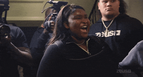 a woman in a zeus sweatshirt is screaming in front of a camera