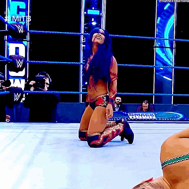 a female wrestler is kneeling down in a wrestling ring while a man is laying on the ground