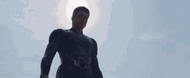 a man in a superhero costume is standing in front of a blue sky with a light coming out of his eyes .