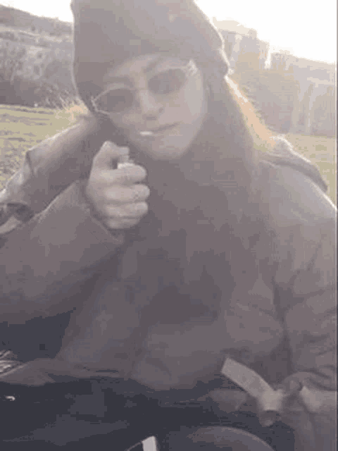 a woman wearing sunglasses and a hat is smoking a cigarette .