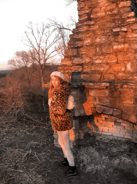 a woman wearing a leopard print coat and a white beret stands in front of a stone wall