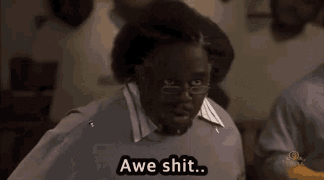 a man with glasses says " awe shit " in front of a group of people
