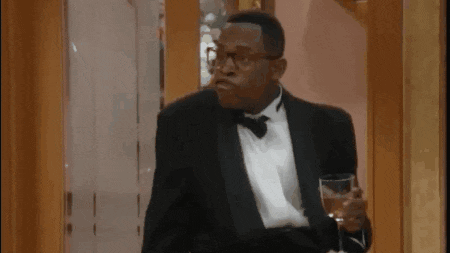 a man in a tuxedo and bow tie is holding a glass of wine and making a funny face .