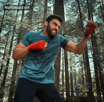 a man in a blue shirt and black pants is standing in the middle of a forest .