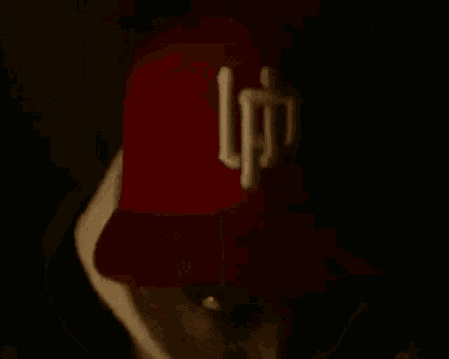 a man wearing a red hat and a white hoodie is looking at the camera in the dark .