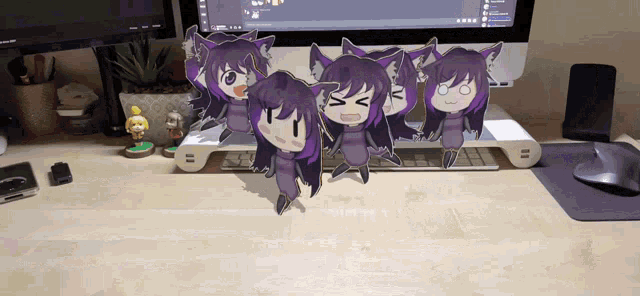 a bunch of anime characters are standing on a desk in front of a computer monitor