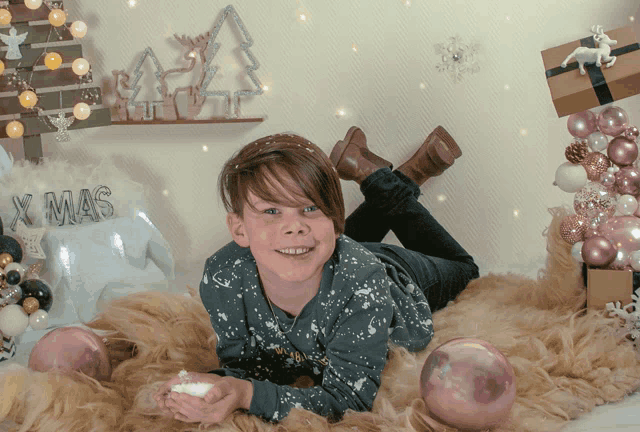 a young boy laying on a blanket with christmas decorations and a sign that says x mas