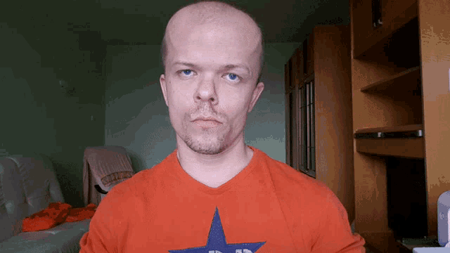 a man wearing an orange shirt with a blue star on it looks at the camera
