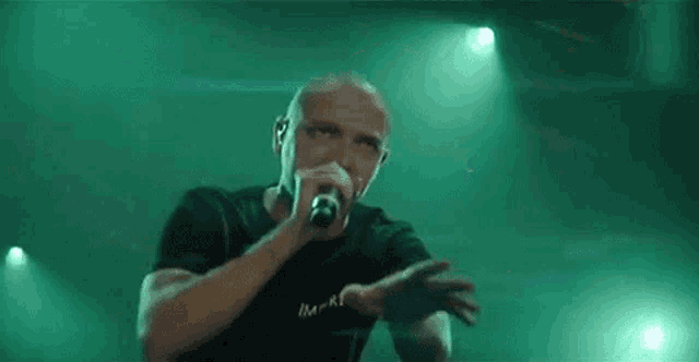a man is singing into a microphone on a stage in front of a green light .
