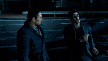 a man smoking a cigarette next to another man in a suit