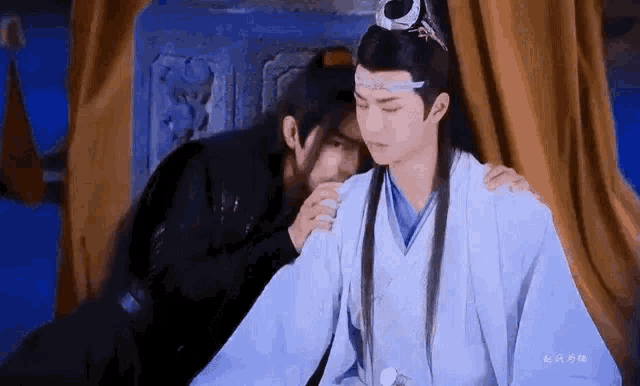 a man is putting his hand on another man 's shoulder while sitting next to each other .