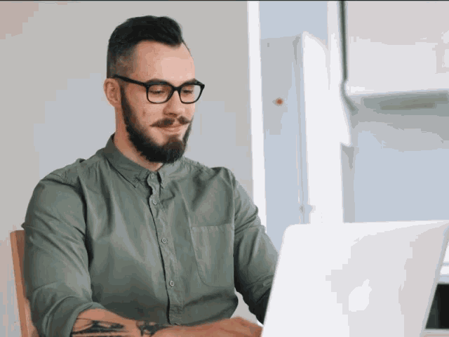 a man with a beard and glasses is using an apple laptop