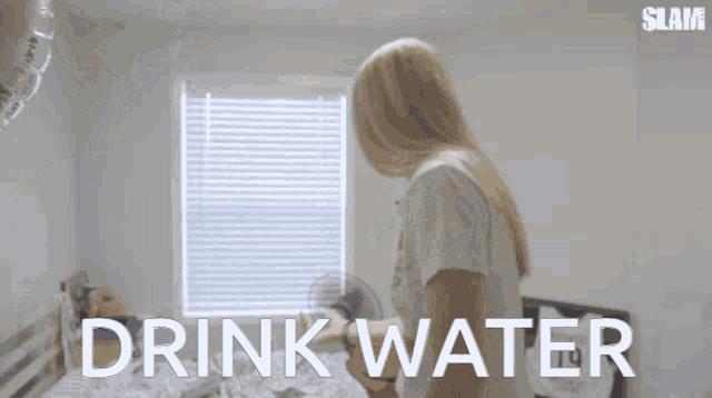 a woman in a white shirt is standing in front of a window with the words drink water written on it