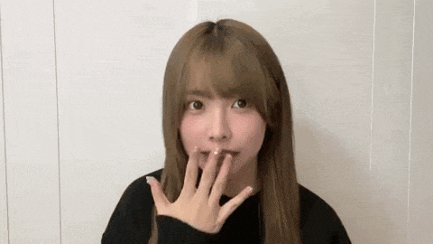 a young woman is covering her mouth with her hand while wearing a black sweater .