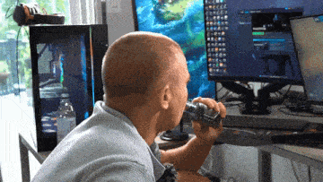 a man drinking water from a bottle while sitting in front of a computer monitor