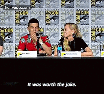 a man and a woman are sitting at a table talking into microphones at a convention .
