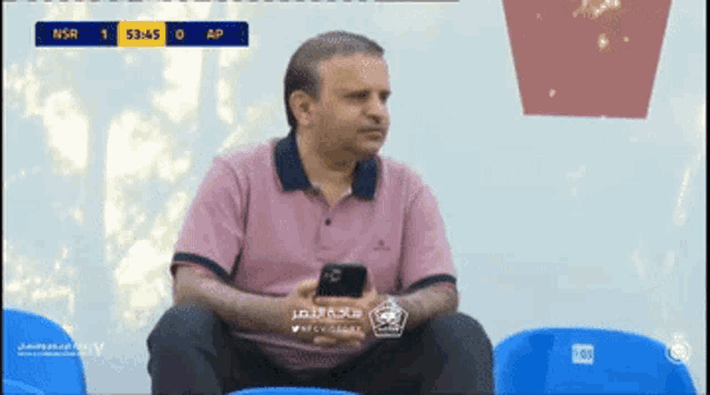 a man sits in a stadium watching a soccer game with a score of 1 to 0
