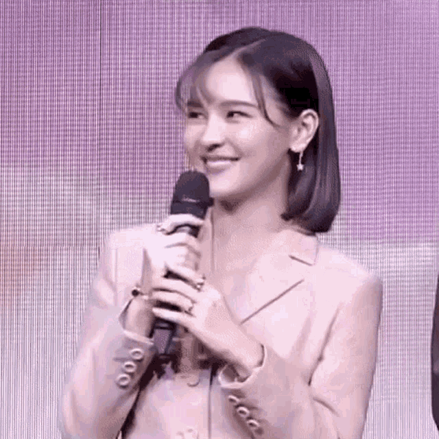 a woman is holding a microphone and smiling while wearing a pink jacket .