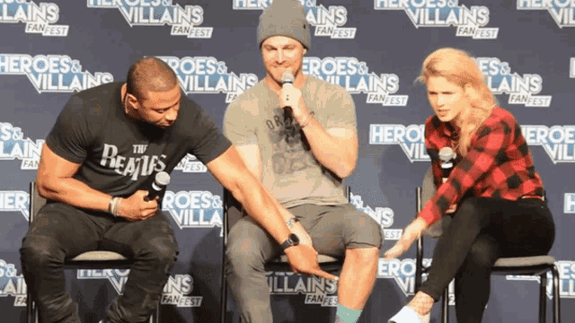 three people are sitting in front of a wall that says heroes and villains