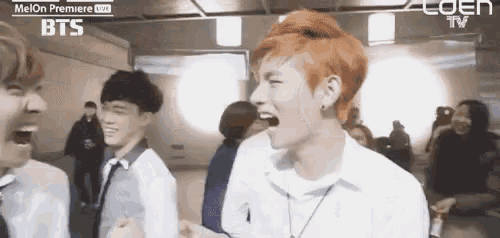 a group of young men are laughing in a room with a sign that says bts on it .