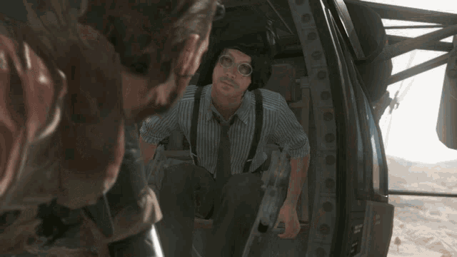 a man in a striped shirt and suspenders is sitting in the back of a helicopter