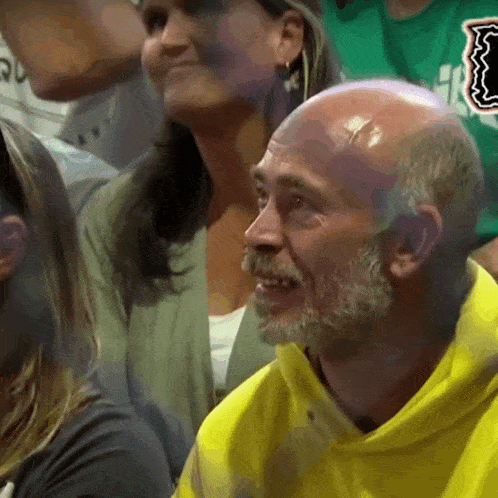a bald man with a beard is wearing a yellow hoodie and smiling