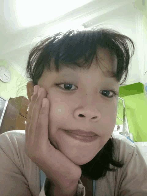 a young girl with her hand on her face looks at the camera