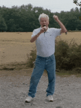 a man singing into a microphone while standing on a dirt road