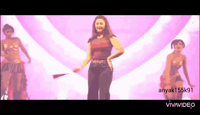 a woman in a red top and black pants is dancing on a stage with two other women .