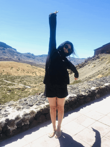a woman wearing sunglasses and a black hoodie is standing with her arms in the air