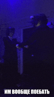 a man in a suit is standing in a dark room with a blue light behind him and a caption in russian