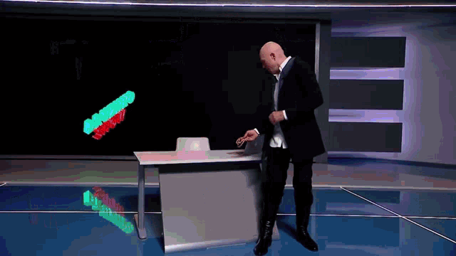 a man in a suit is standing in front of a desk with a green and red sign that says ' a ' on it