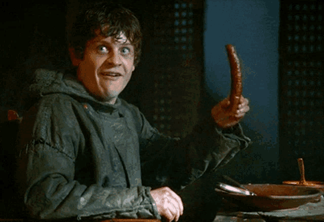 a man is holding a sausage in his hand and smiling